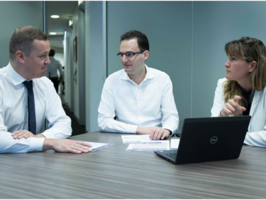 three people sitting at a desk conversing