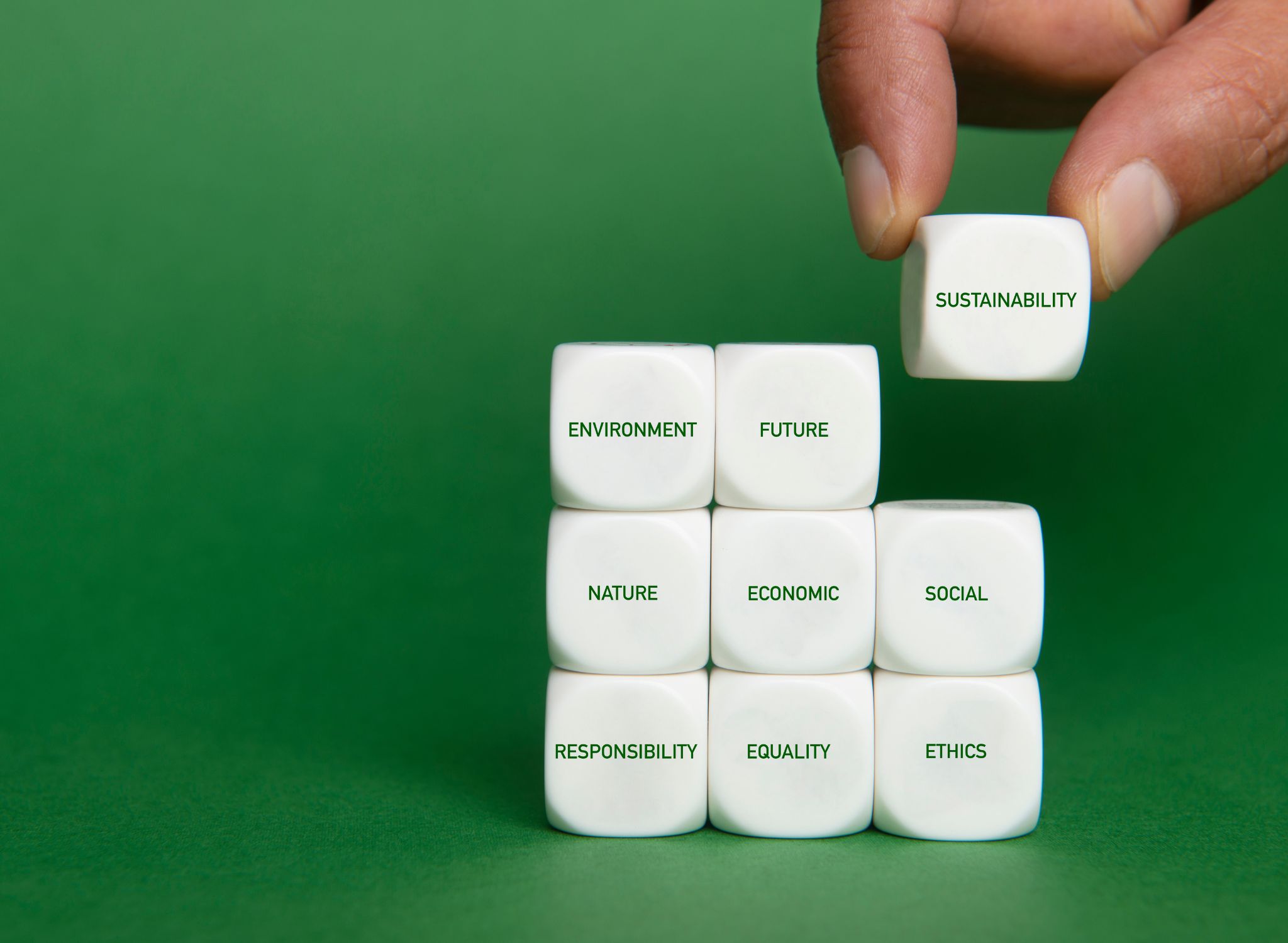 A hand holding a 'Sustainability' block poised to complete a larger cube of growth factors, symbolising the integration of climate considerations into real estate investment strategies