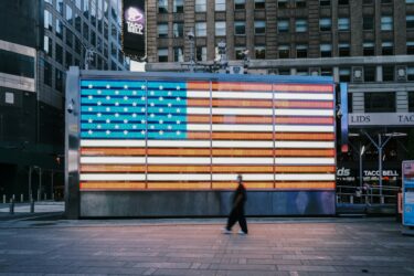 a person walking on a sidewalk with a large United States flag displayed behind them.