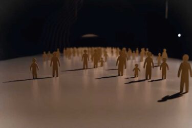 A conceptual image showing numerous small, stylized human figures standing on a smooth surface, casting long shadows under dramatic lighting. The figures gradually fade into the darkness in the background, symbolizing an uncertain or evolving demographic future.
